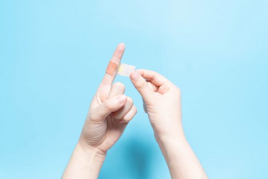 Young female have injured index finger and putting adhesive bandages plaster for first aid on light blue background. Health care and medical concept.